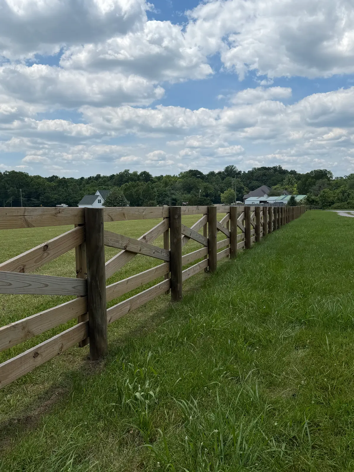 Four-board wood pasture fence stretching across a Middle Tennessee farm under a blue sky