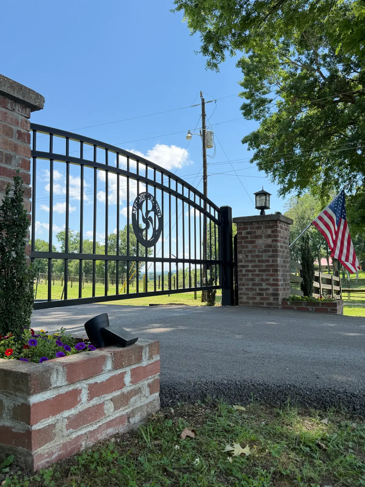 Black ornamental driveway gate on brick columns with an American flag