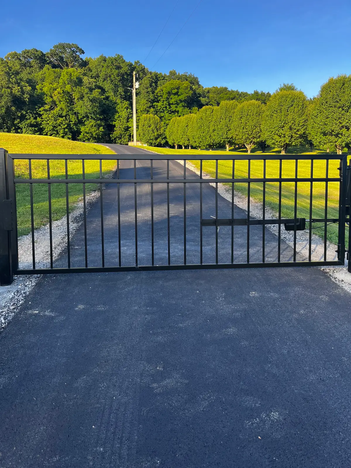 Black double swing driveway gate across a gravel drive